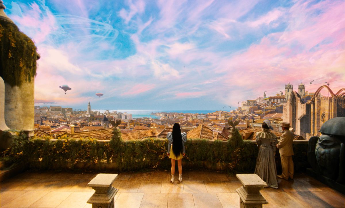 Emma Stone as Bella Baxter stands before a fantastical, colorful view of the city of Lisbon in Poor Things