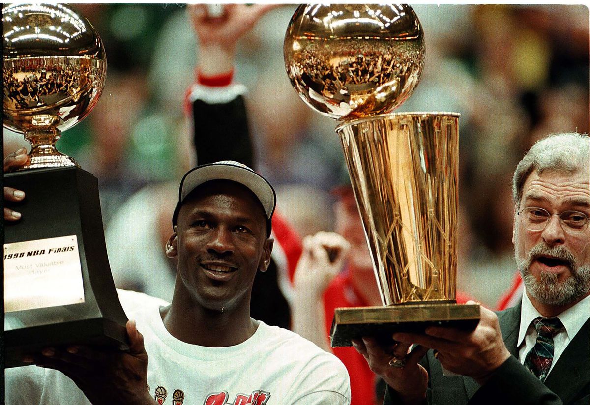 Michael Jordan holds his MVP finals trophy while Phil Jackson holds the NBA championship trophy in 1998.