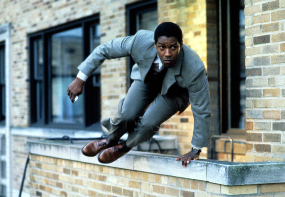 Denzel Washington, wearing a suit, jumps over a ledge in The Pelican Brief.
