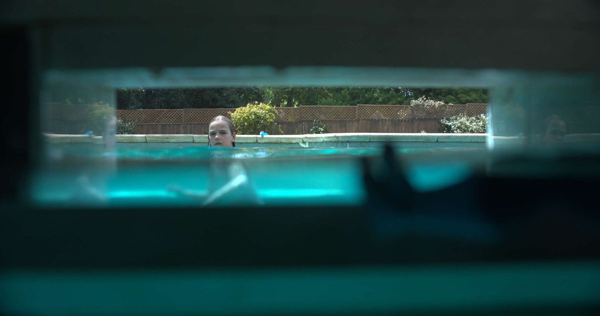 A kid looks toward a pool skimmer, which we see from the skimmer’s perspective in Night Swim