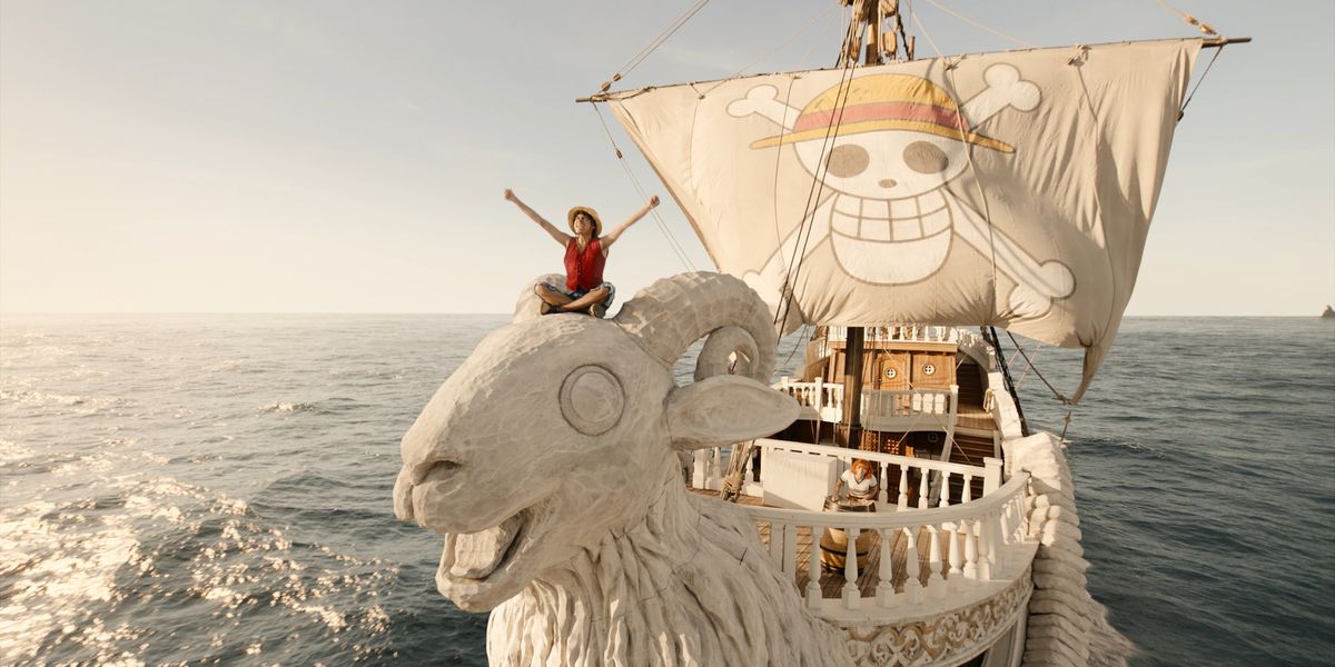 Luffy (Iñaki Godoy) sits on the head of the sheep mast of the Going Merry and cheers in a still from One Piece