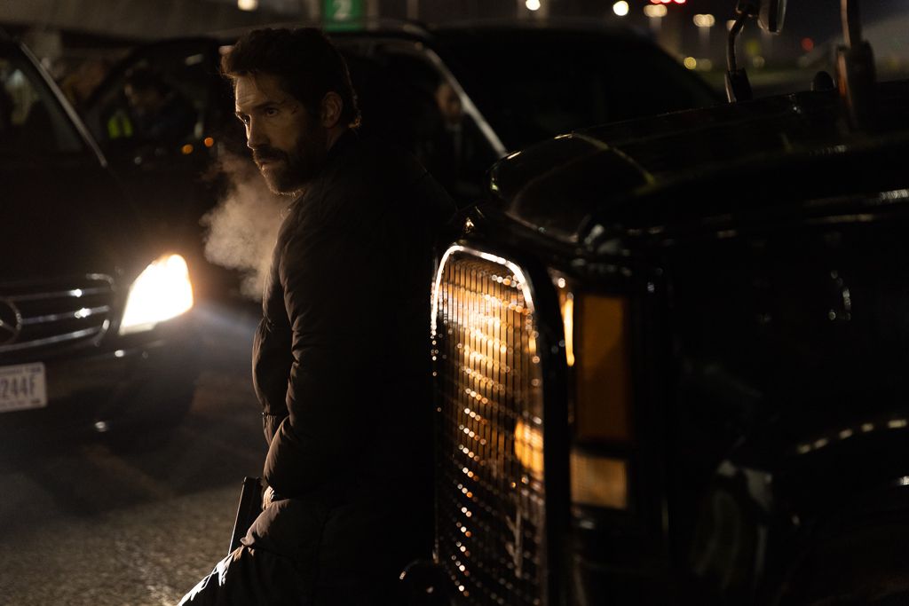 Scott Adkins leans against the front of a car as you can see his breath exhaled in the cold weather in One More Shot