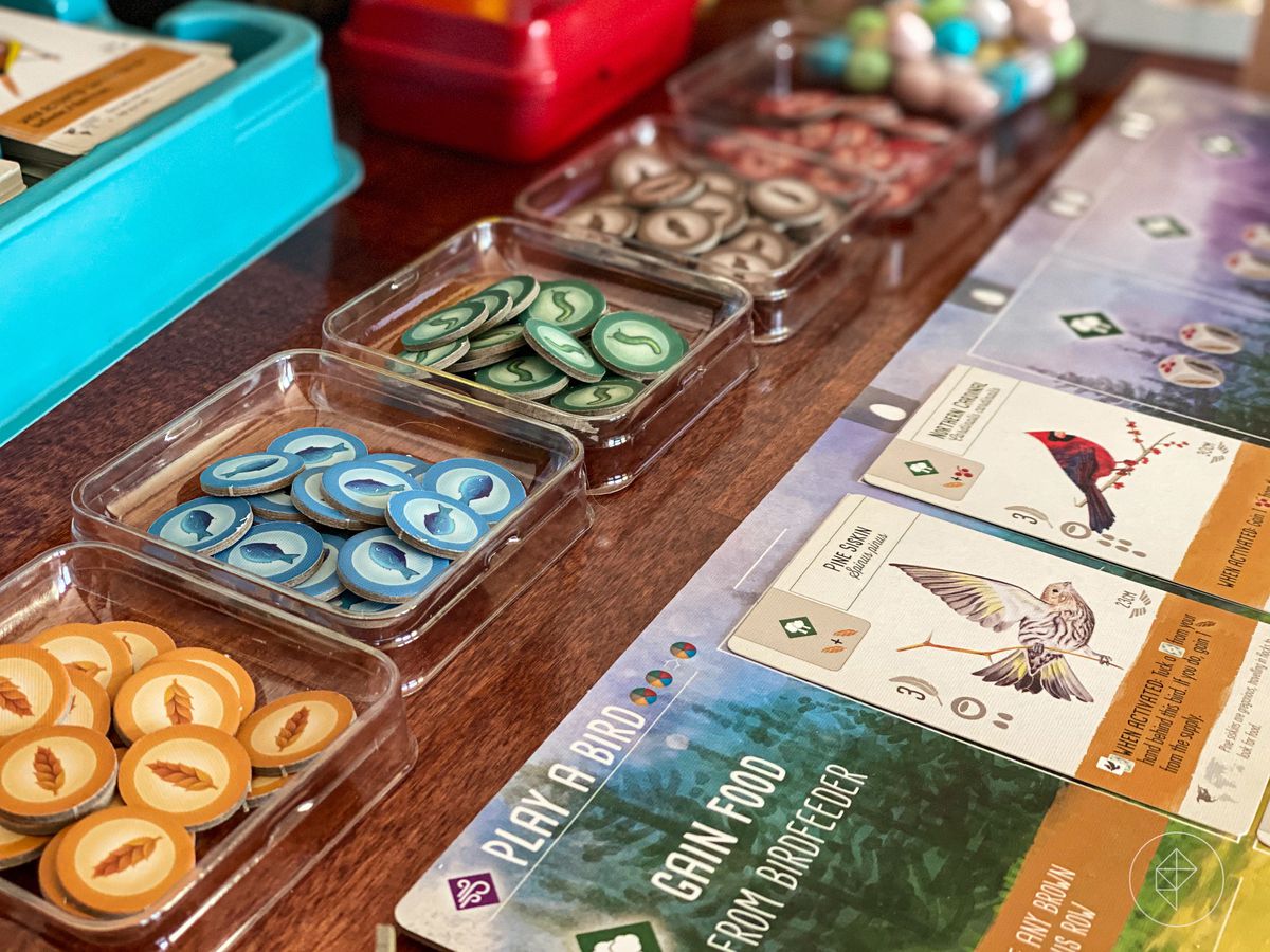 A selection of tokens in plastic trays, with cards filled with bird art along the sideboard.