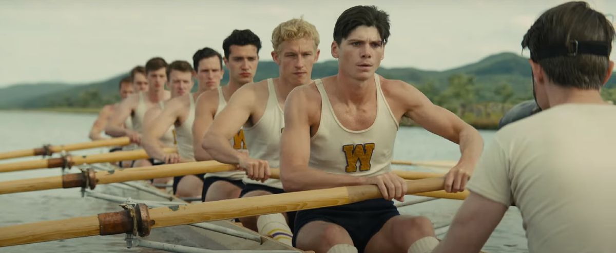 A boatful of men rowing across a lake.