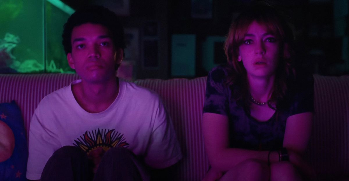 Teenagers Owen (Justice Smith) and Maddy (Brigette Lundy-Paine) and sit together in the dark on a couch, staring into an off-screen TV, their faces lit by a purple light in Jane Schoenbrun’s movie I Saw the TV Glow