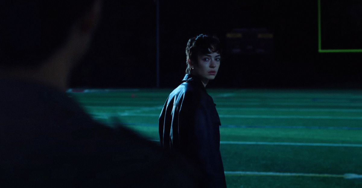 Maddy (Brigette Lundy-Paine) stands on her high-school’s football field at night and looks over her shoulder at her friend Owen (Justice Smith, seen in silhouette) in Jane Schoenbrun’s movie I Saw the TV Glow 