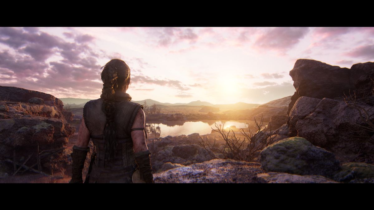 Hellblade 2’s Senua stands looking at a beautiful sunrise over a rugged landscape
