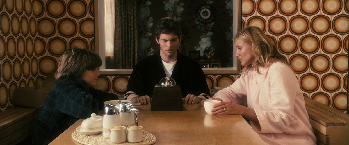 Cameron Diaz, James Marsden, and Sam Oz Stone sit around their dining table, all looking at the box from The Box.