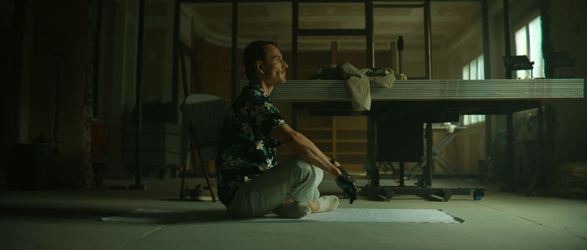 Michael Fassbender as The Killer sits cross-legged on the floor on a plastic sheet