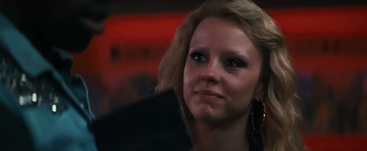 Maxine (Mia Goth) stands next to Leon (Moses Sumney) in his video store, with a vivid red background behind them, in Ti West’s Maxxxine