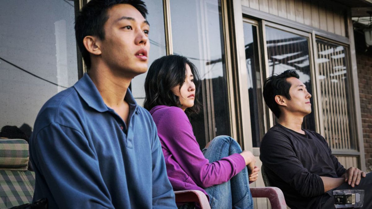 Yoo Ah-in, Jeon Jong-seo, and Steven Yeun sit on a the front porch of a small house in Burning