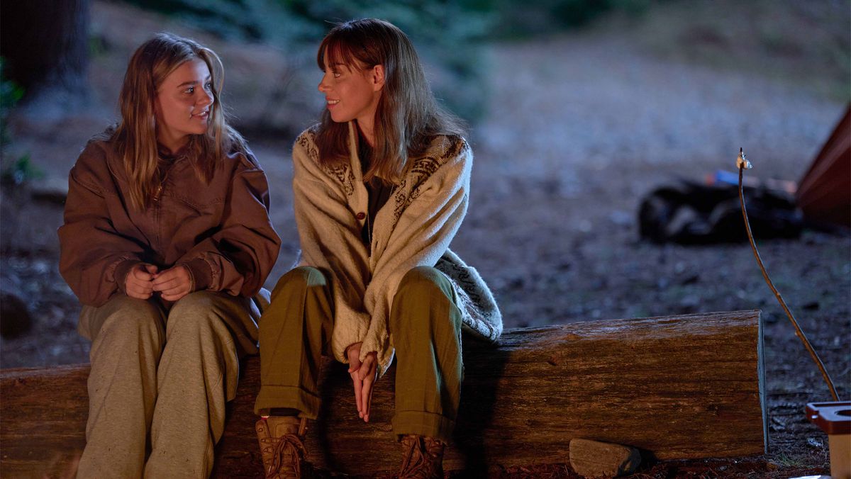 Maisy Stella and Aubrey Plaza sitting on a log in the woods with a tent in My Old Ass