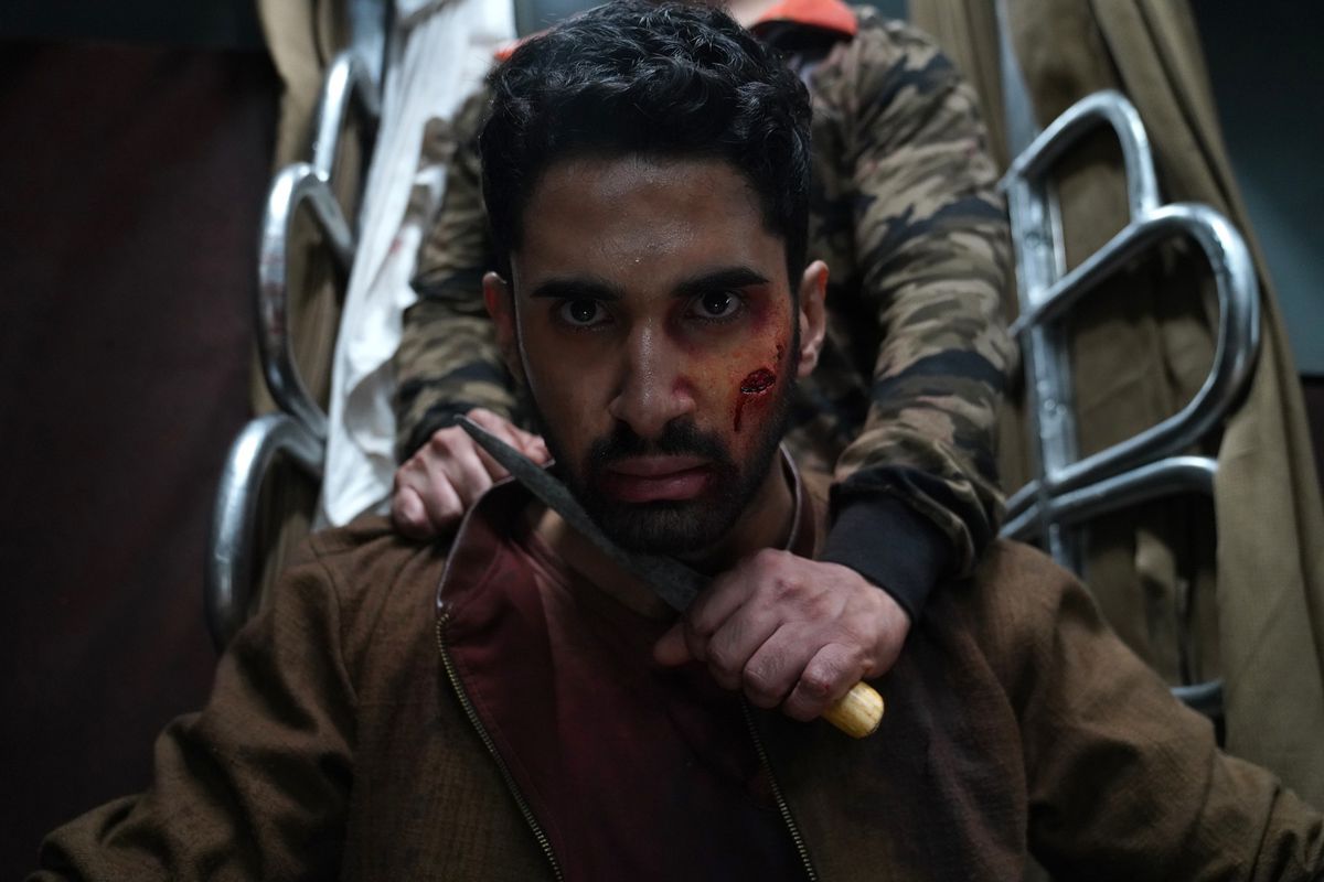 Lakshya as Amrit in Kill. His face is bloodied and another person behind him is holding a knife to his neck. 