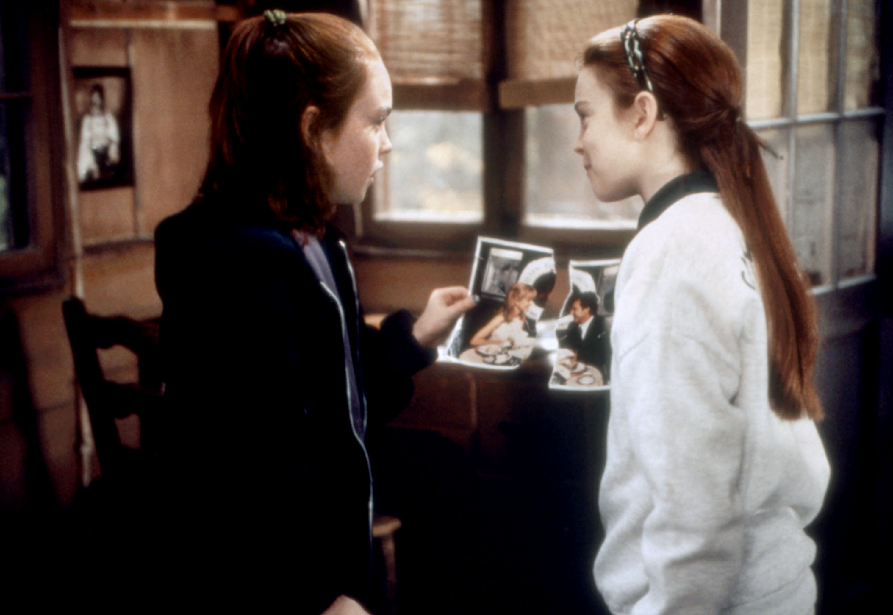 Two young Lindsay Lohans hold up torn halves of a picture together in The Parent Trap