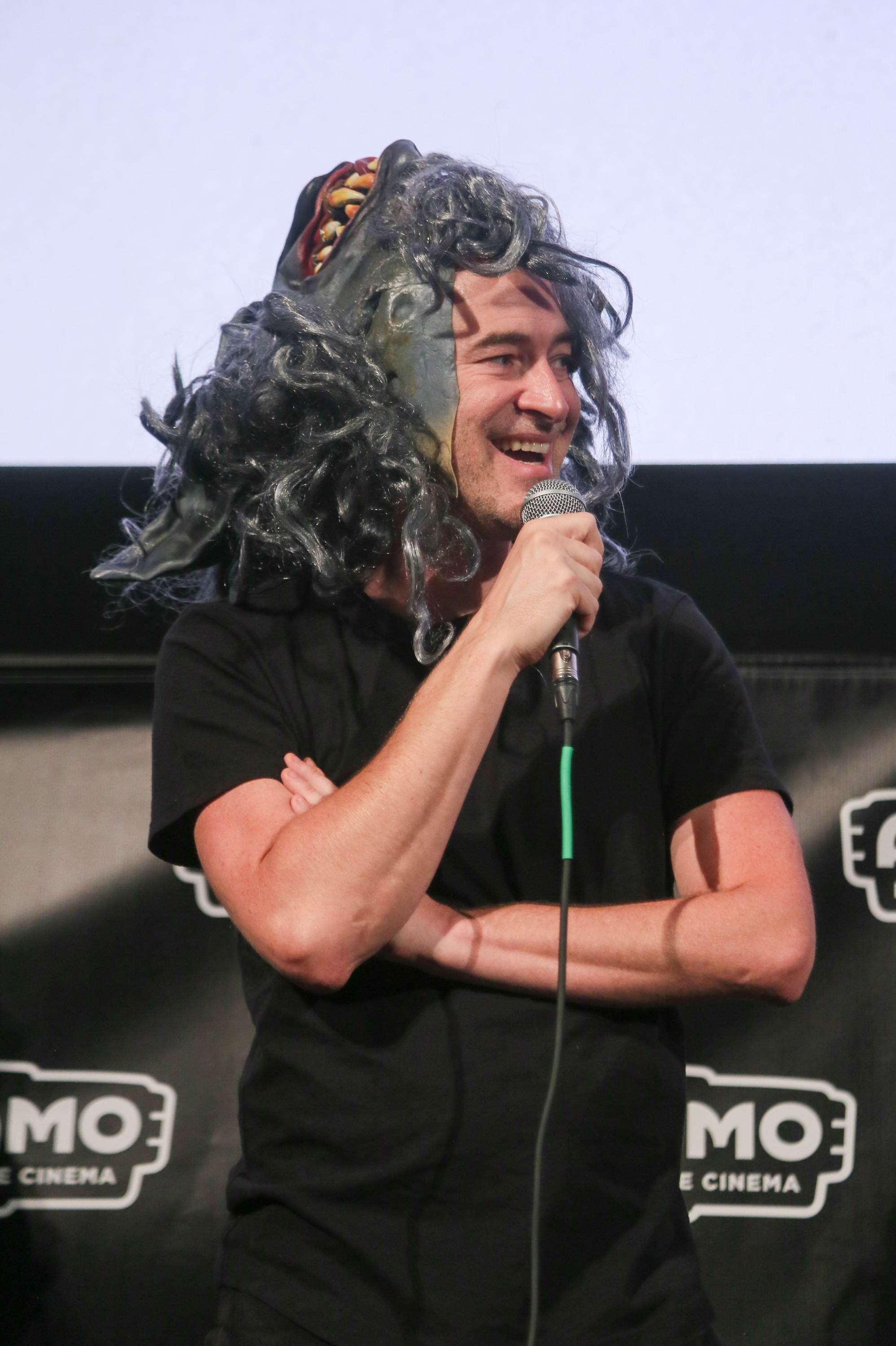 Mark Duplass with the Peachfuzz werewolf mask pushed back on his head, holding a microphone and smiling at the Q&A after The Creep Tapes’ premiere at Fantastic Fest 2024