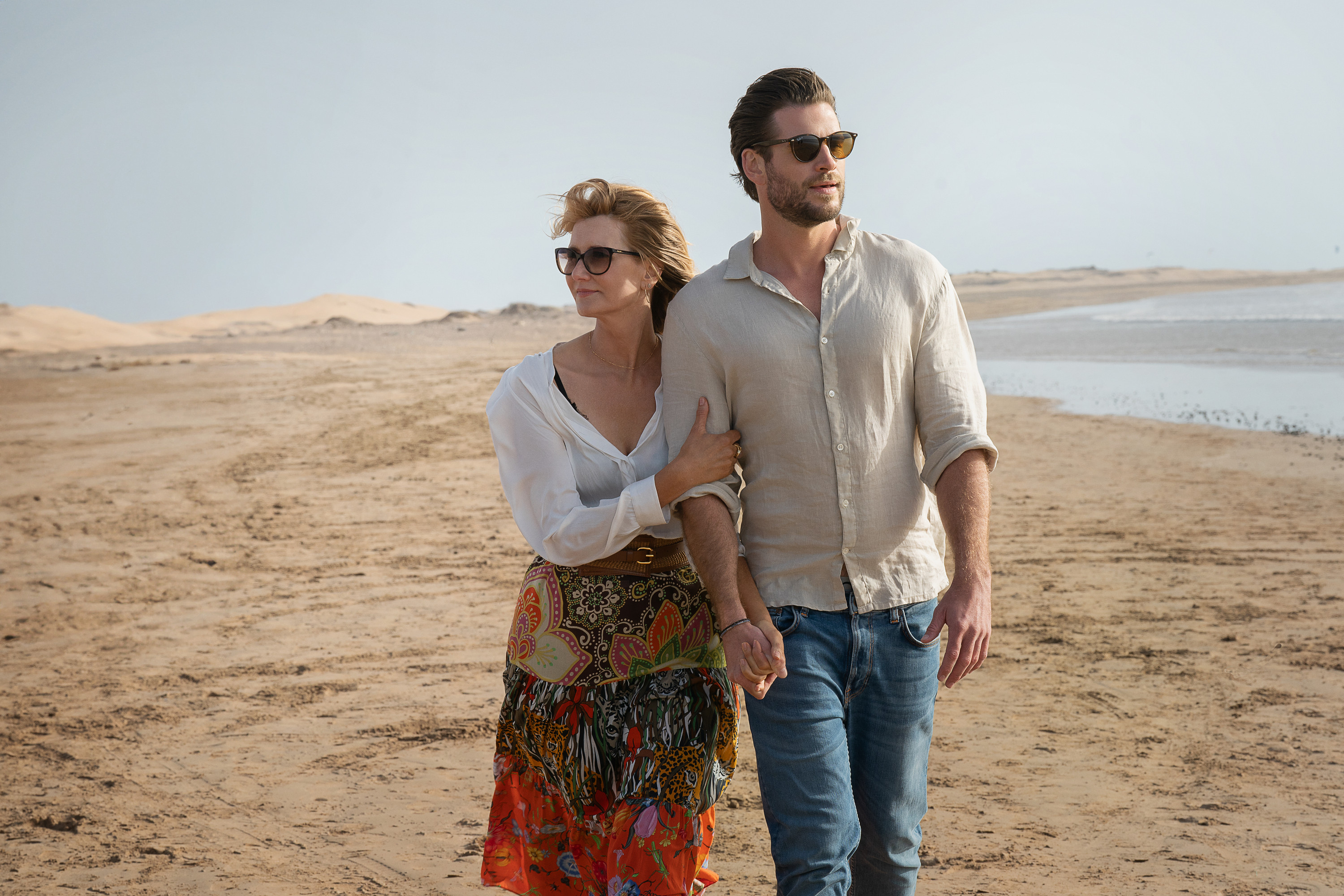 A woman (Laura Dern) and a man (Liam Hemsworth) walking hand-in-hand along a shore in Lonely Planet.