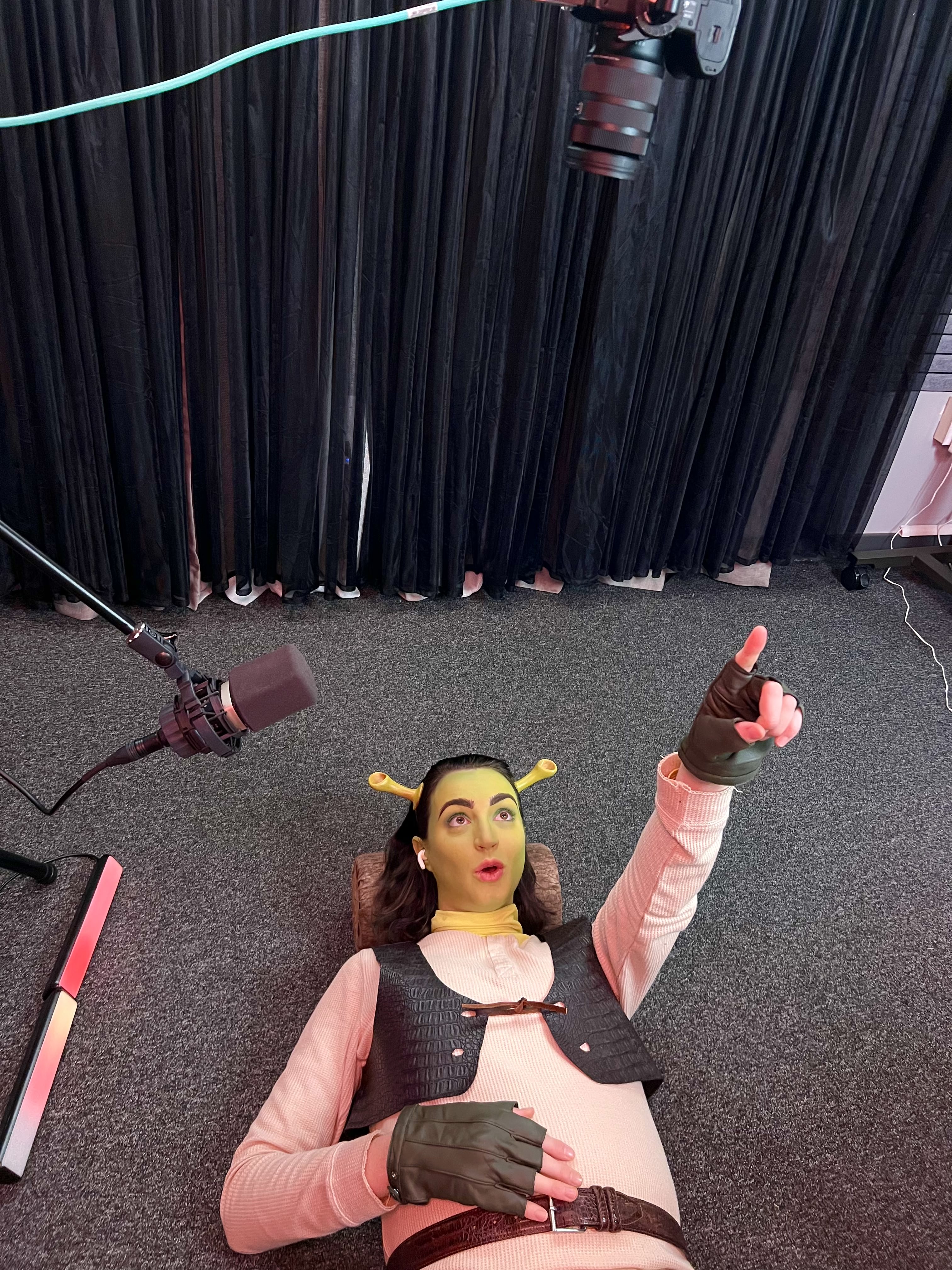 Gibi ASMR lays on the ground with a microphone. She is dressed as Shrek