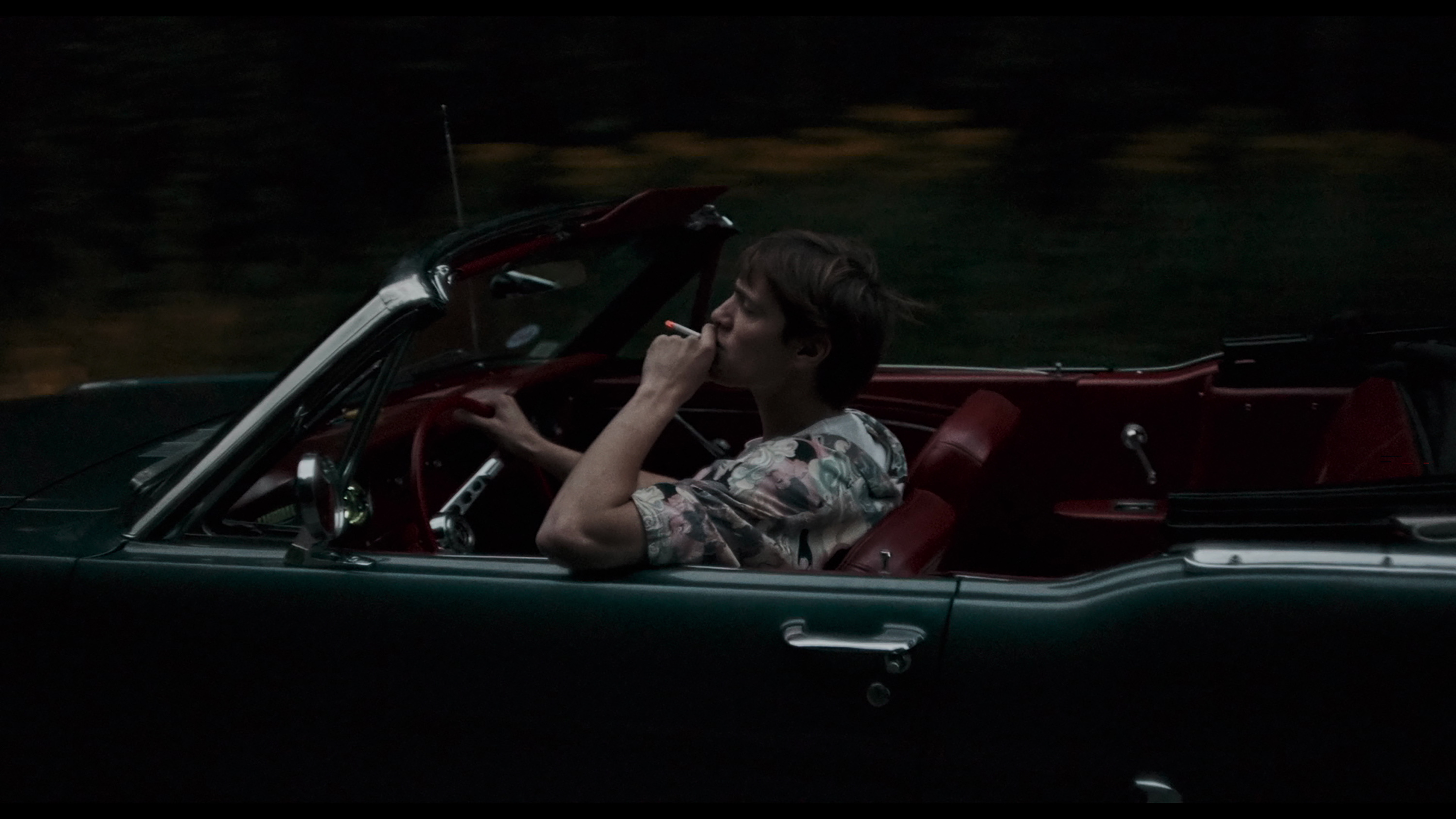 A young man takes a drag on a cigarette while casually driving a large green classic convertible in the French horror-thriller MadS