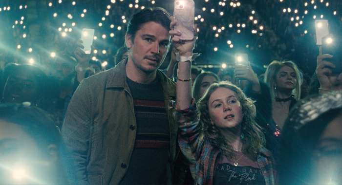 Cooper (Josh Hartnett) stands amid a sea of Lady Raven fans, including his daughter, holding up their phones at a concert