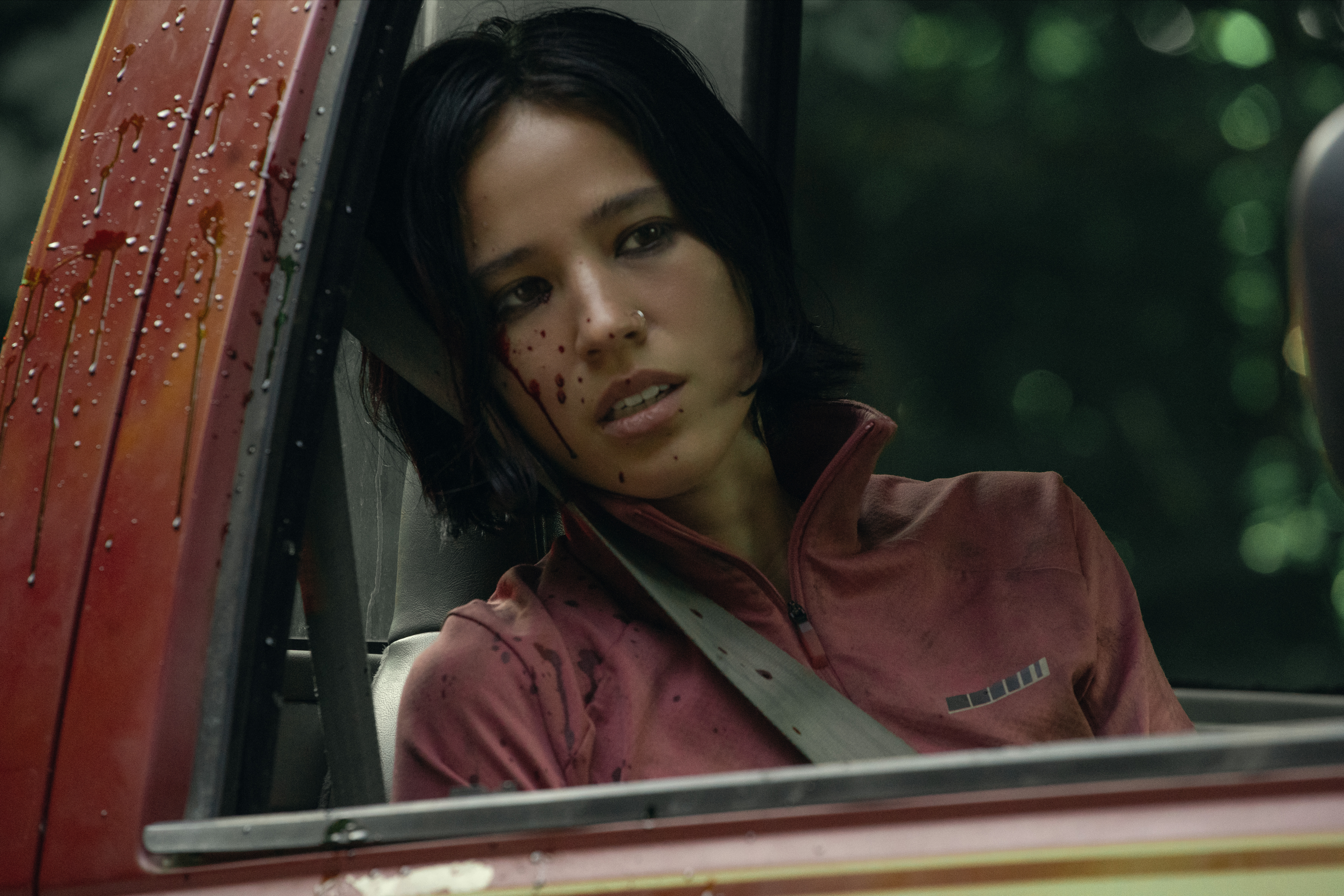 A woman (Kelsey Asbille) in a beige tracksuit sitting in the passenger seat of a vehicle covered in blood in Don’t Move.