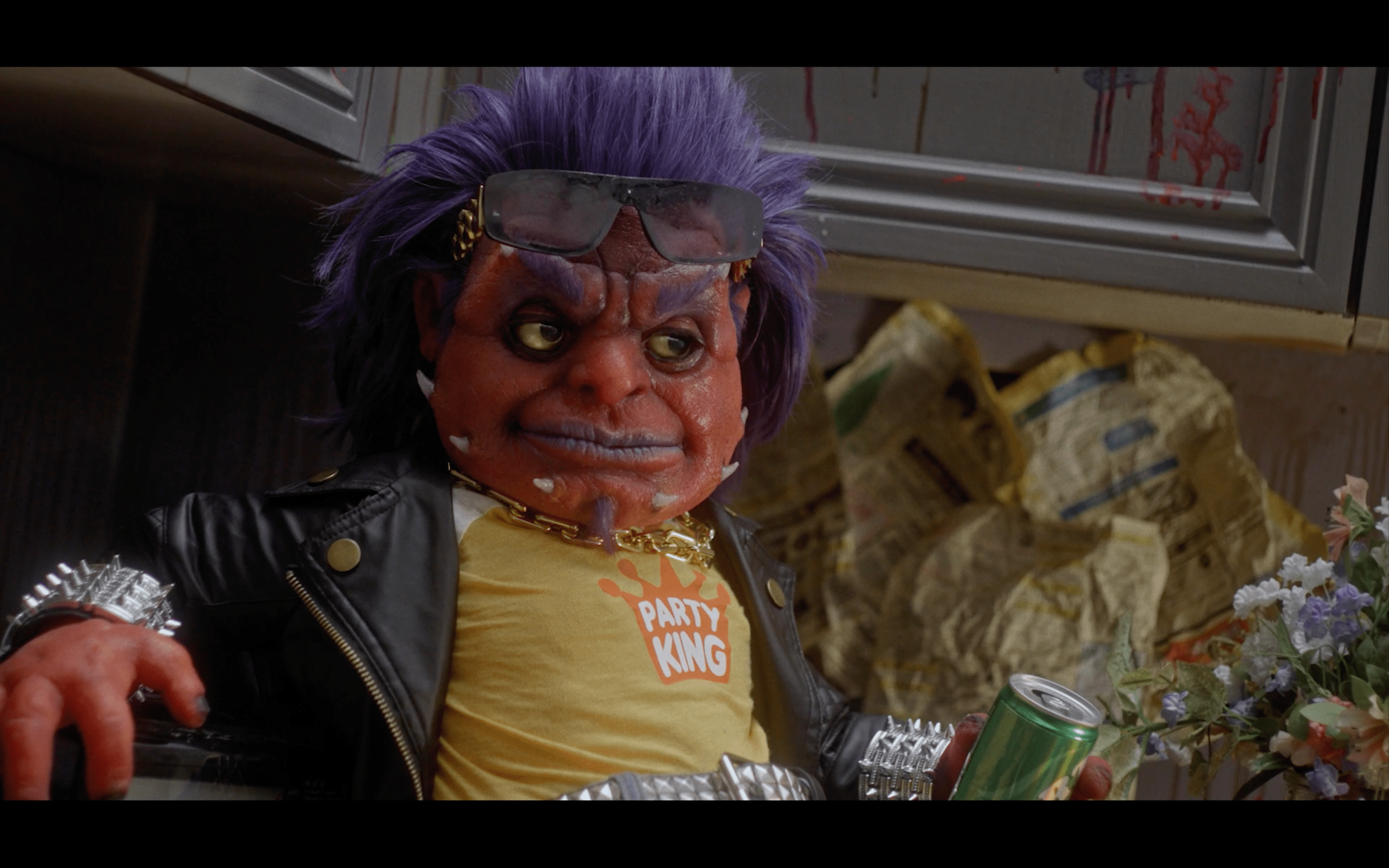 Frankie Freako, an orange gremlin-like creature in biker attire, holding a can of soda in a trashed kitchen in Frankie Freako.