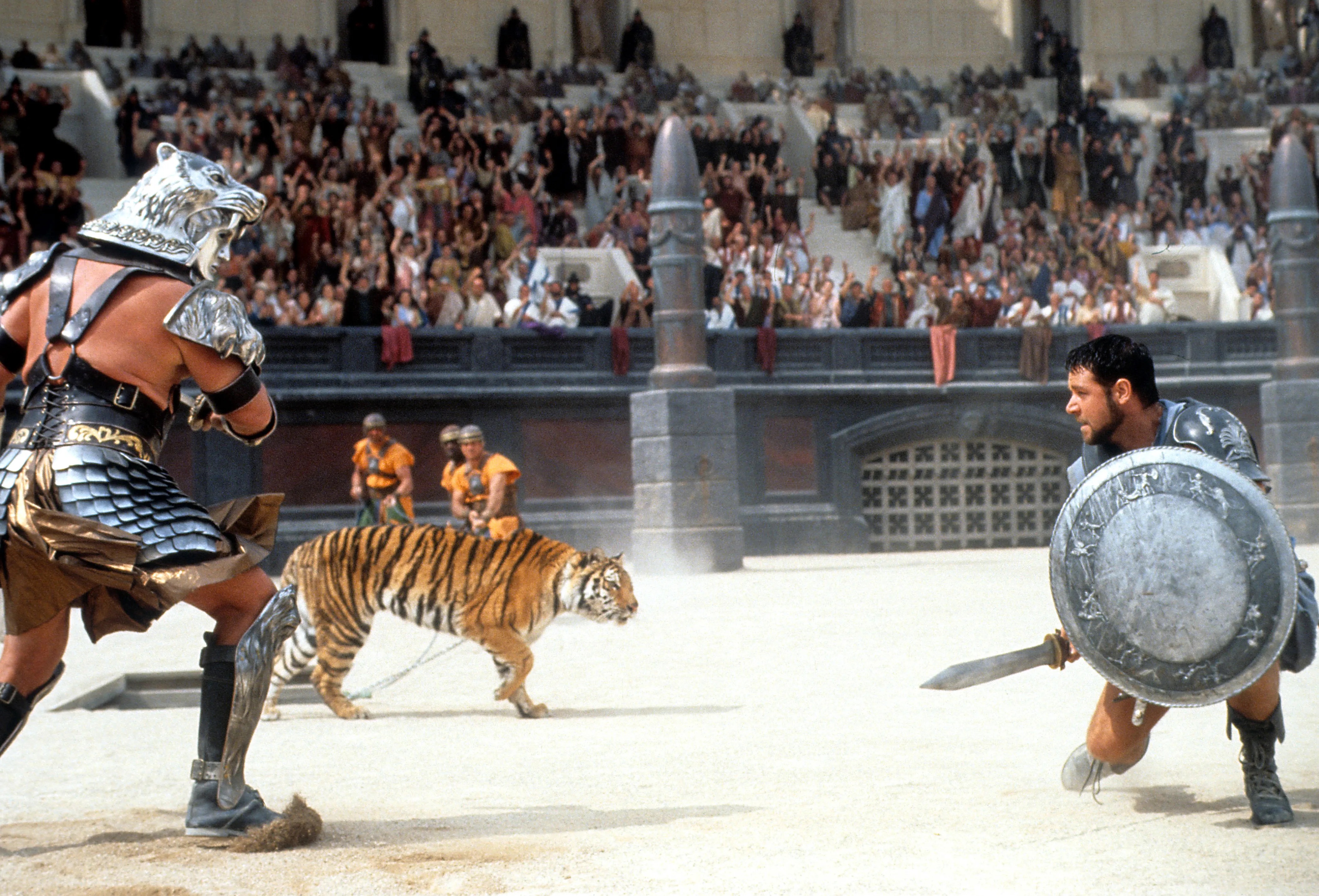 Gladiator Maximus (Russell Crowe) crouches in the sand of the Colosseum as he’s charged by a tiger and a helmeted warrior in 2000’s Gladiator 