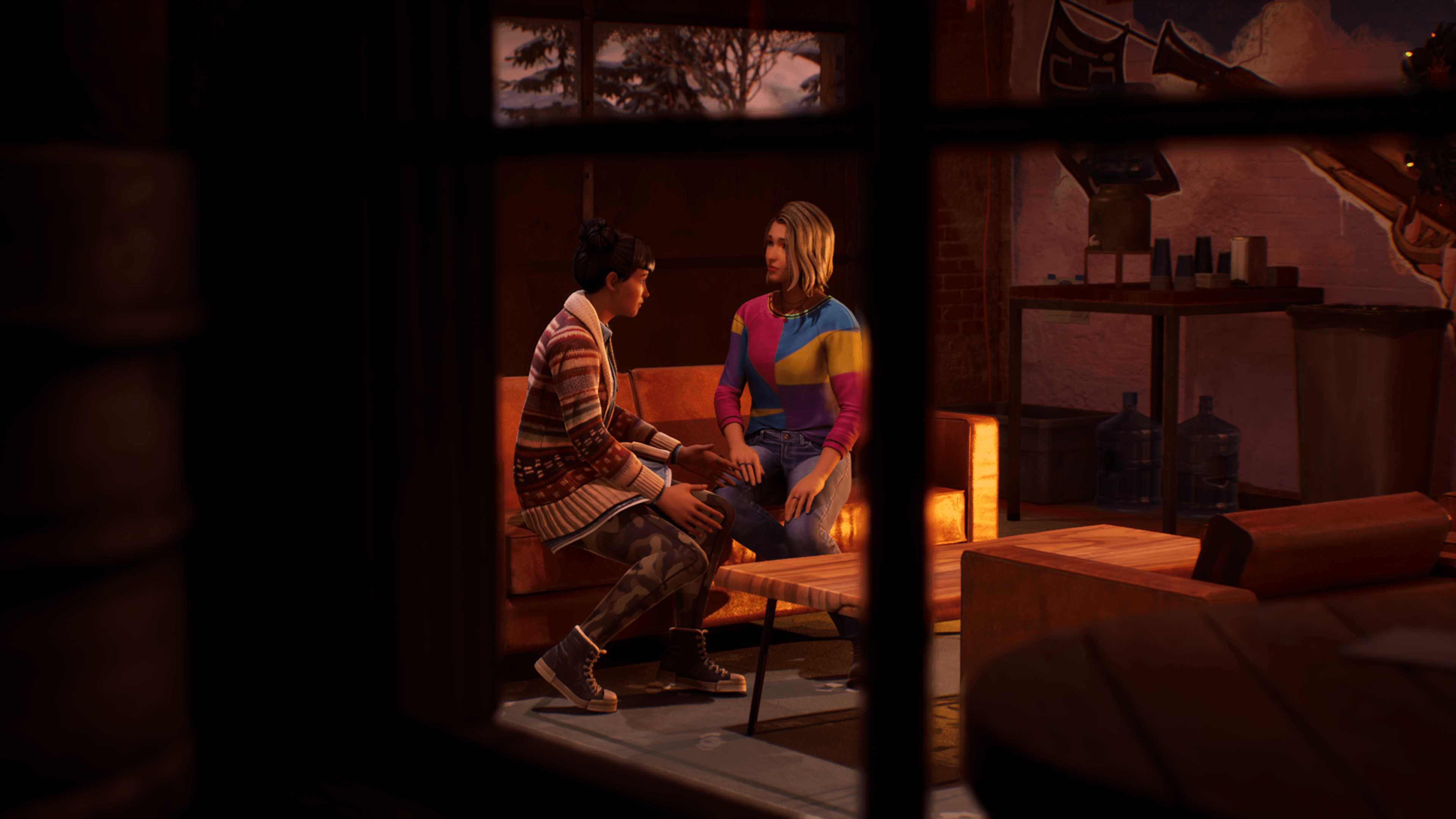 Two characters from Life Is Strange: Double Exposure sit on a couch, talking to each other. The viewer is seeing this image from outside of the building the characters are in, through a window.