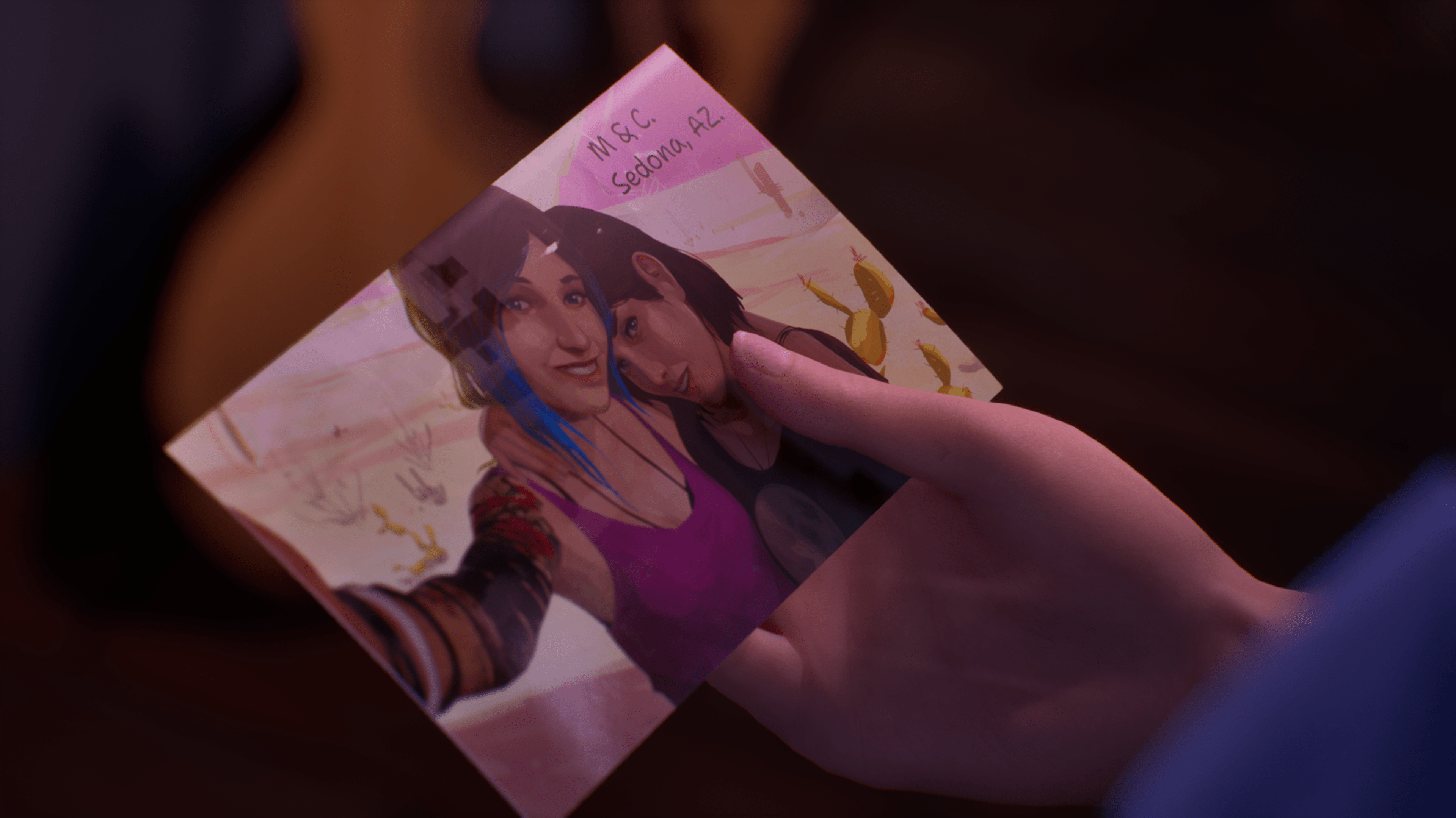 A zoomed-in look at a character’s hand holding a photograph depicting two people smiling and posing for a selfie in Life Is Strange: Double Exposure