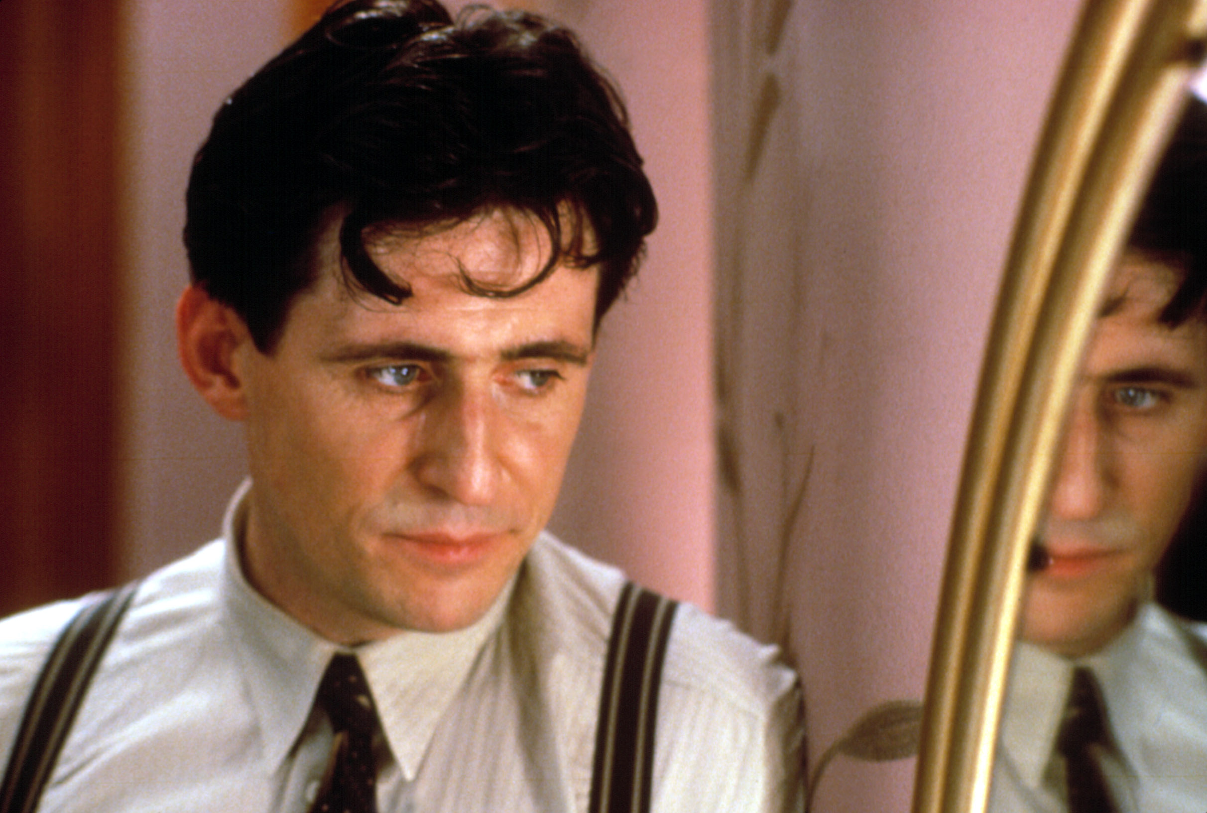 Gabriel Byrne looks off-camera thoughtfully in Miller’s Crossing, with his reflection in the mirror also looking away on the other side of the frame