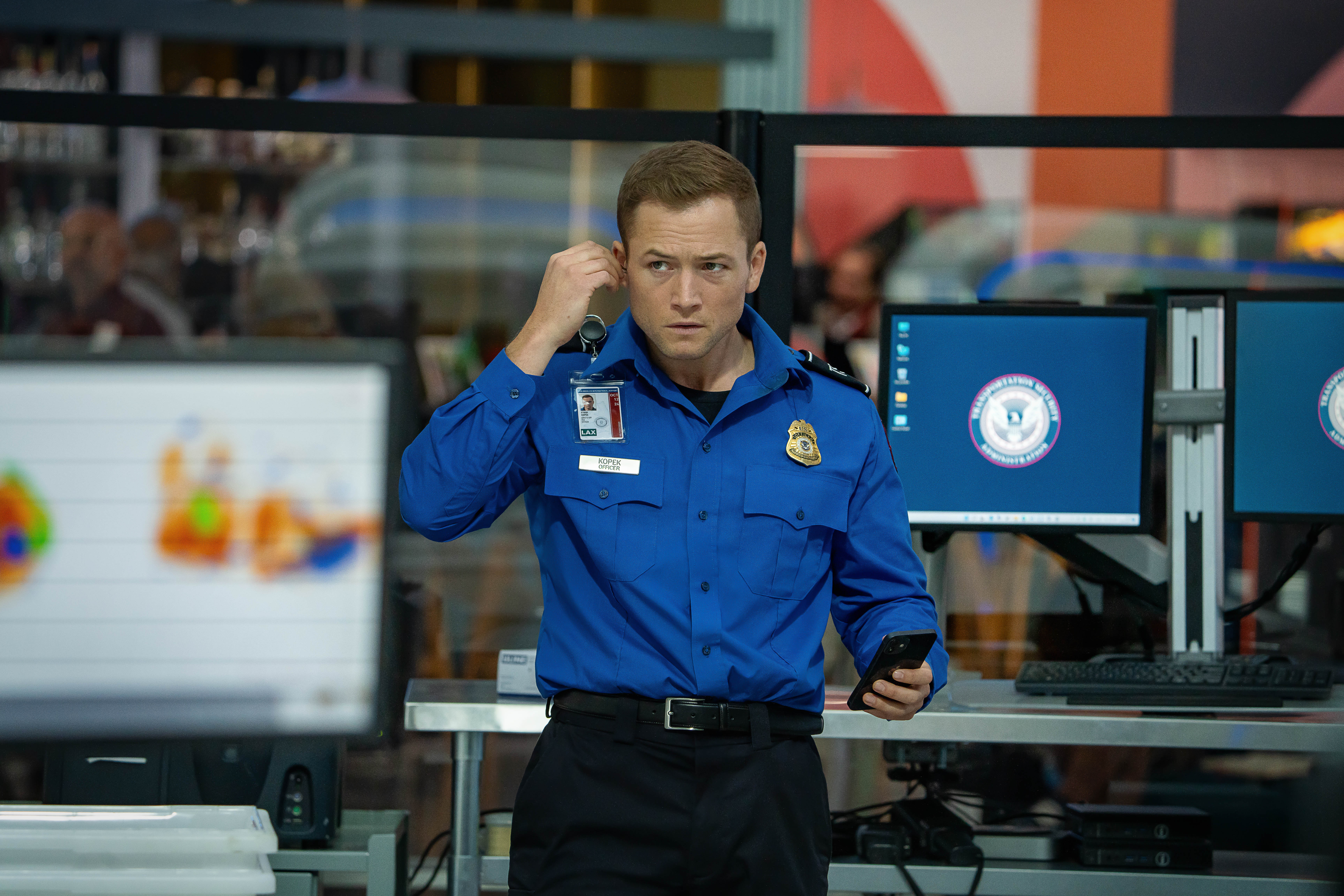 Taron Egerton puts in an earpiece as a TSA agent in Carry-On