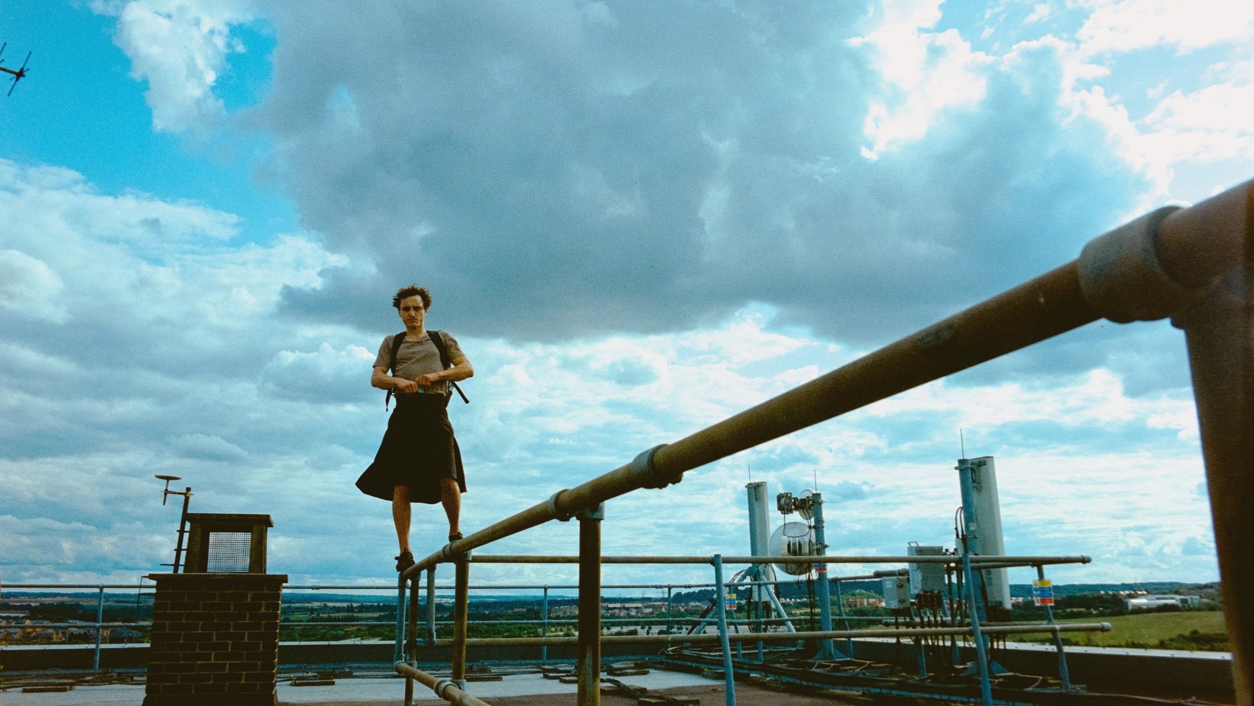 Franz Rogowski standing on a pipe with a cloudy sky in the background in Bird