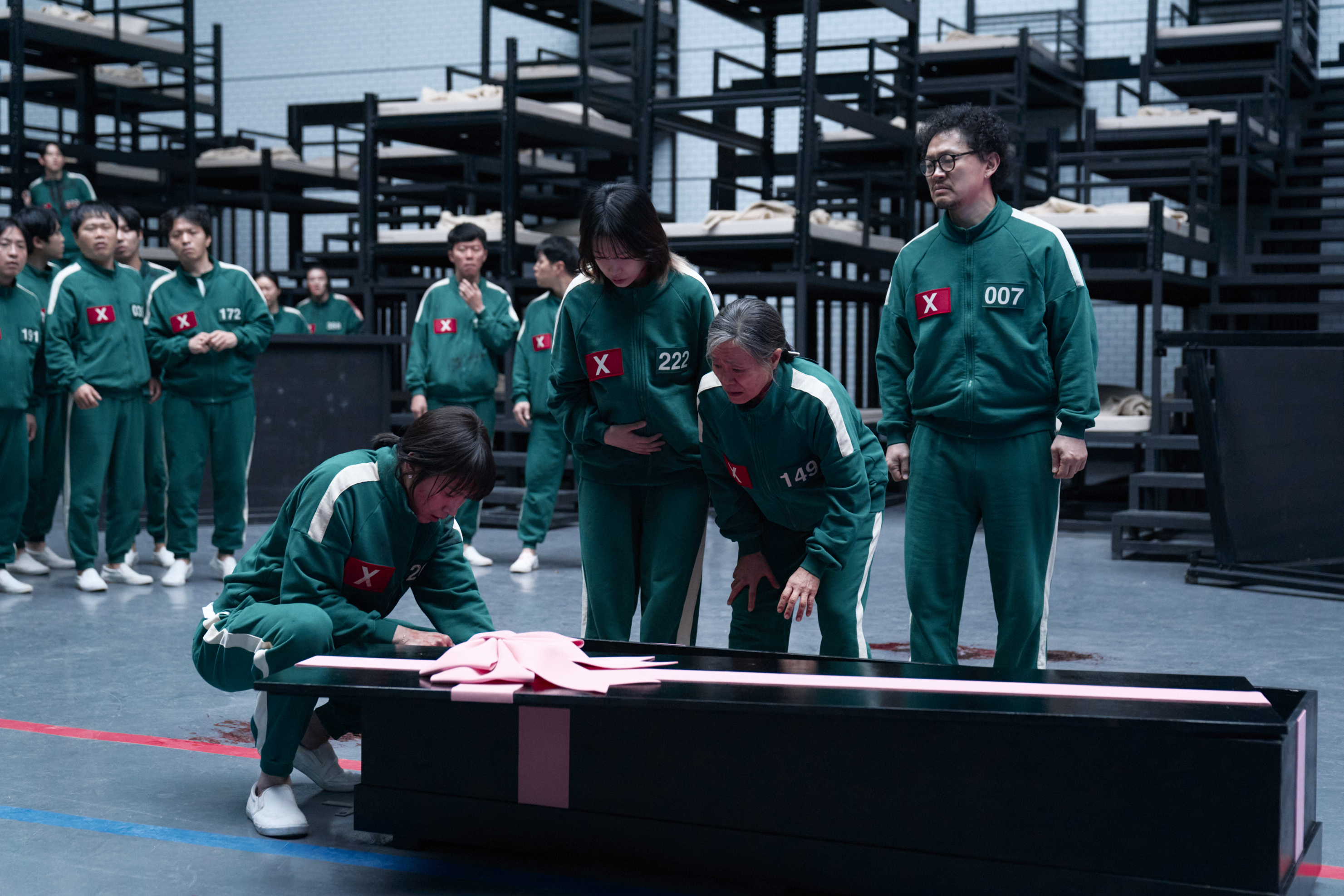 A group of remaining Squid Game contestants gather around a gift-wrapped coffin in a still from season 3