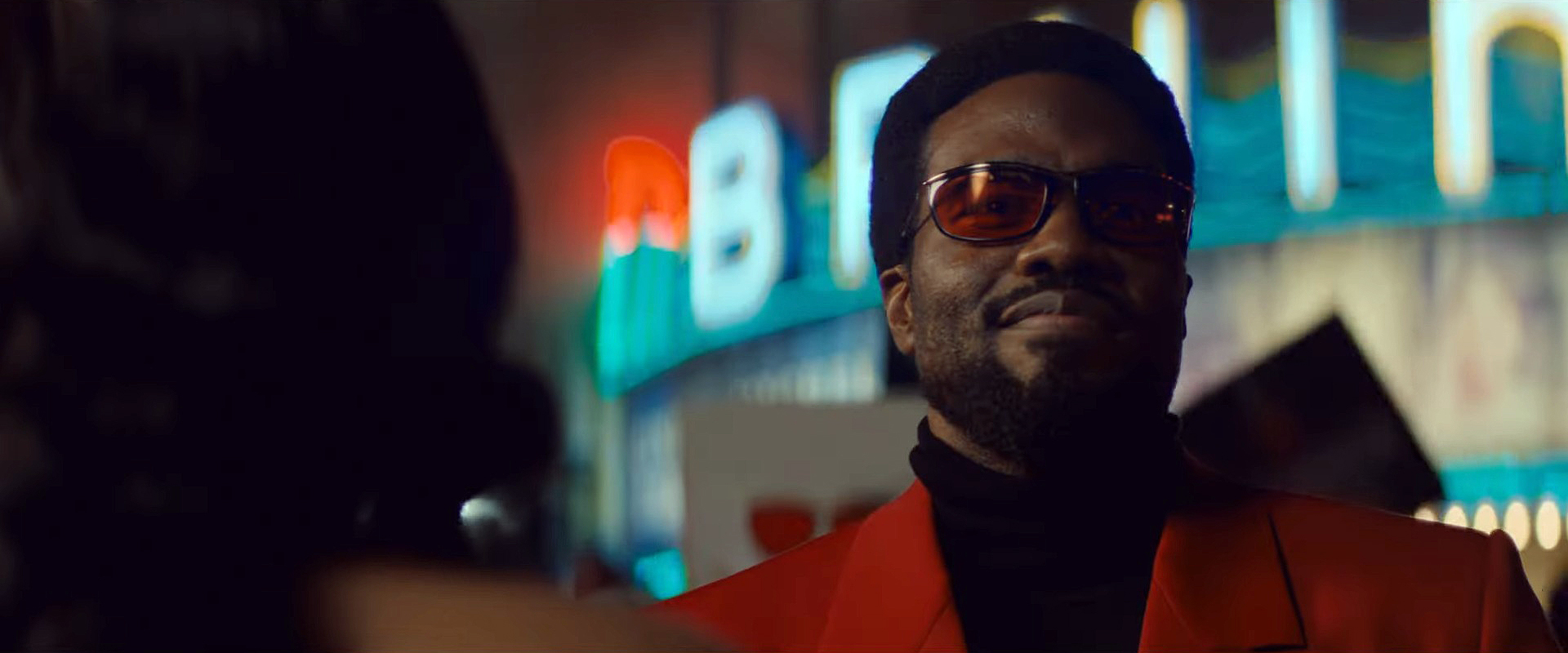 Simon Williams, Wonder Man, played by Yahya Abdul-Mateen II, grins confidently while wearing sunglasses, a black turtleneck and red suit jacket in a still from Wonder Man