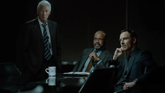 Three men in a still from The Agency season 1 sitting at a table looking stunned