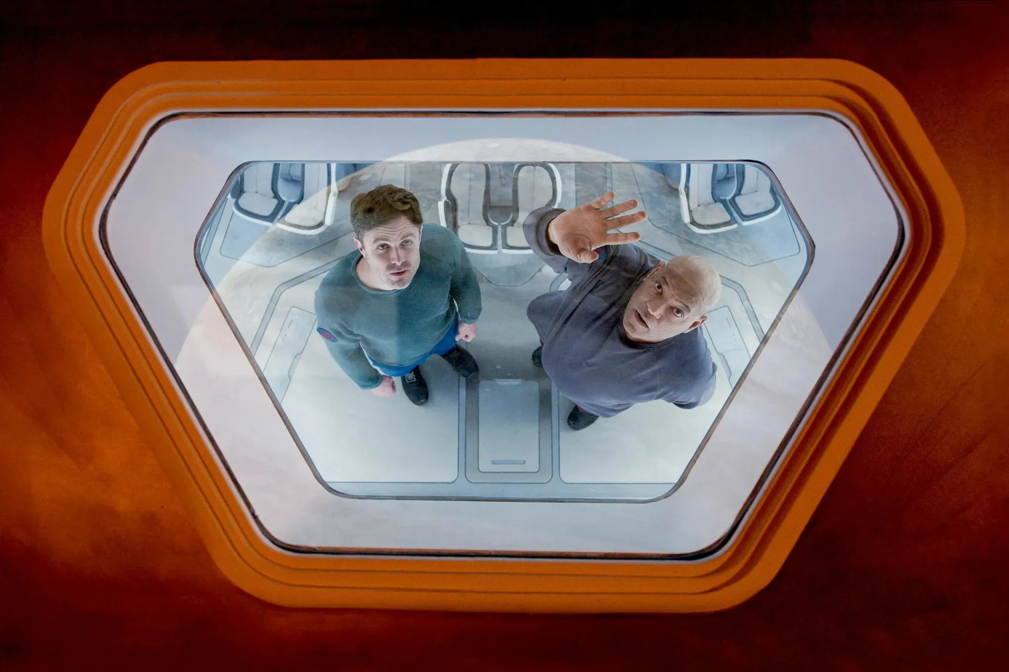 Casey Affleck and Laurence Fishburne staring through the porthole of a spaceship in Slingshot