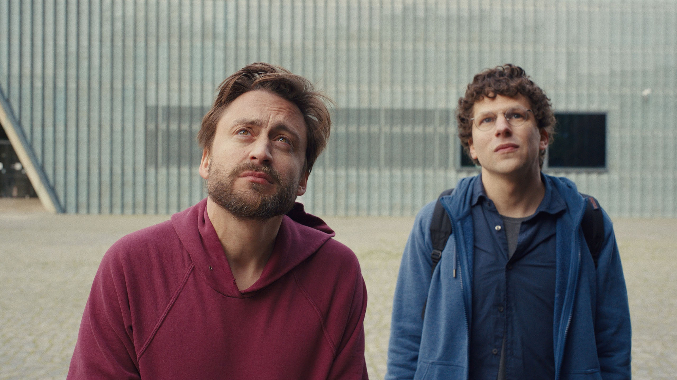 Kieran Culkin and Jesse Eisenberg stand outside looking up at something in A Real Pain