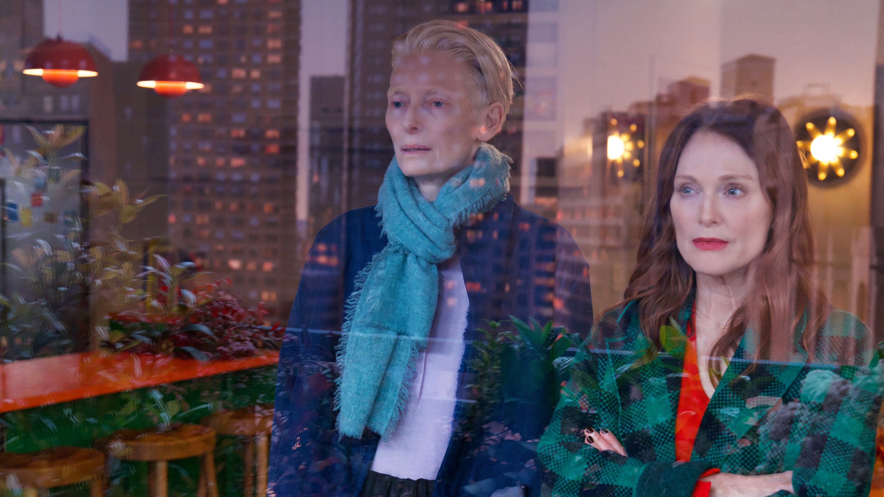 Tilda Swinton and Julianne Moore standing in front of a window in The Room Next Door.