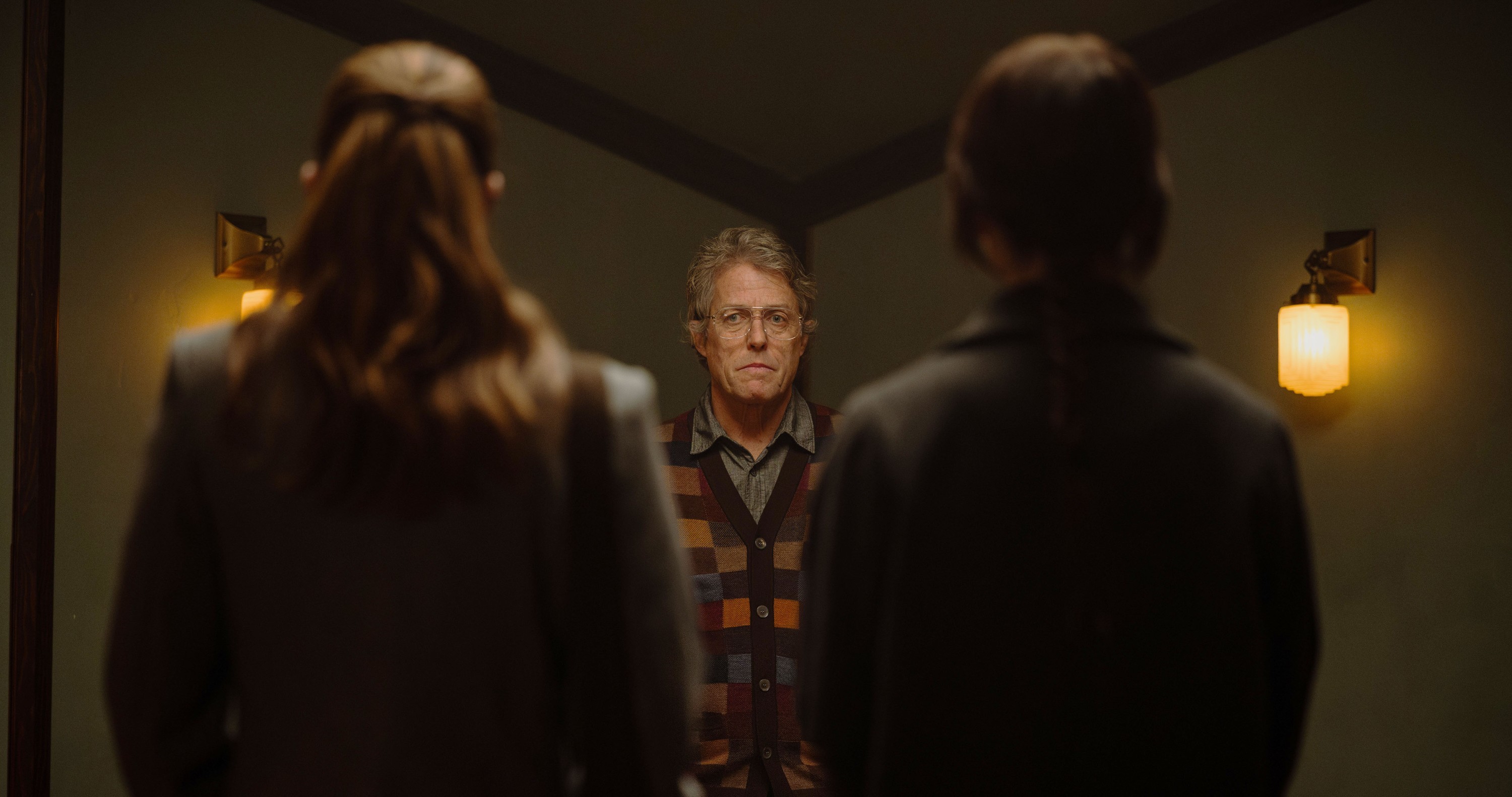 Mr. Reed (Hugh Grant) thoughtfully examines the two women (both nearly in silhouette, with their backs to the camera) that he’s trapped in his house in Heretic