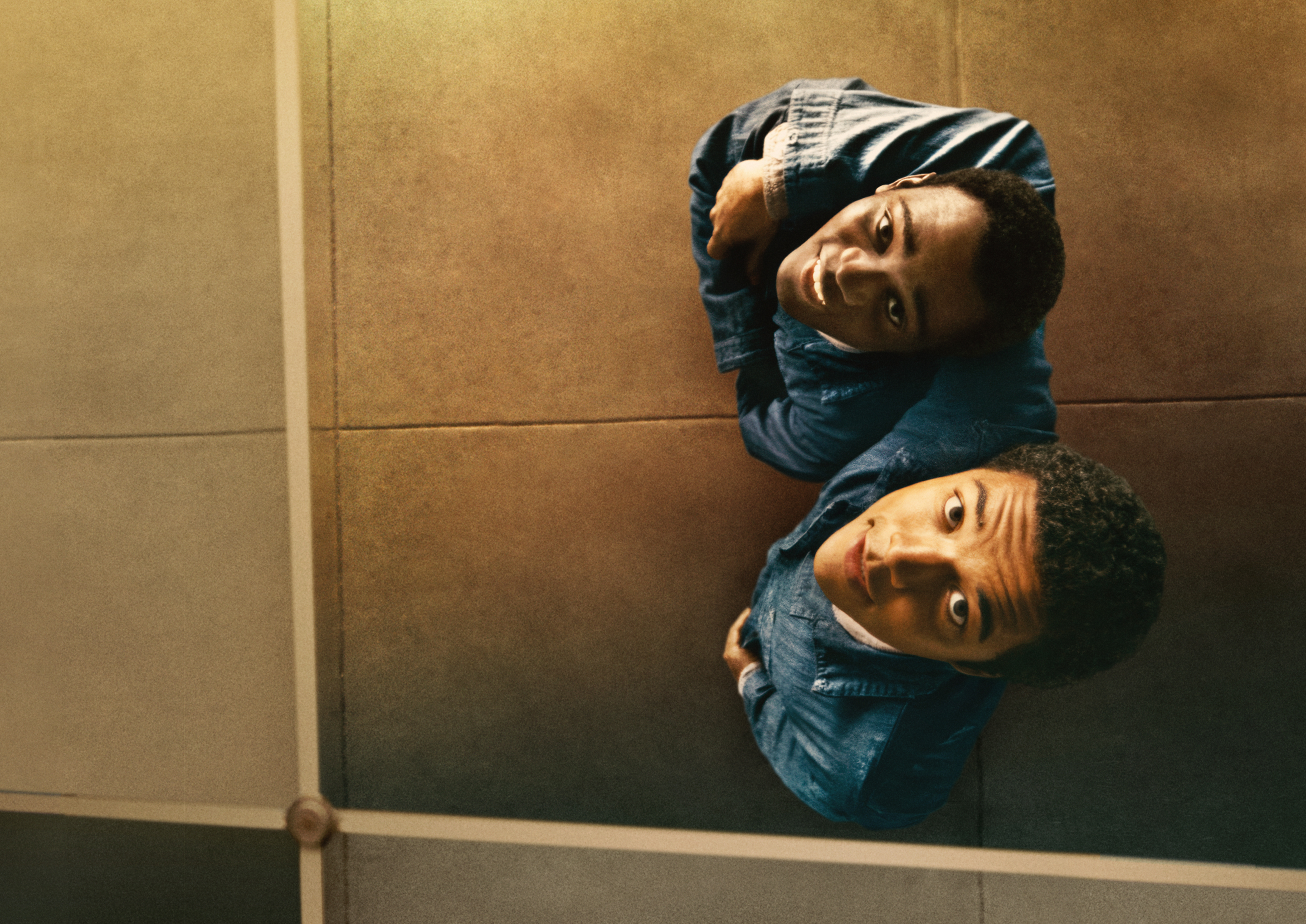 Two men in jean jackets looking up at their reflection and smiling in Nickel Boys.