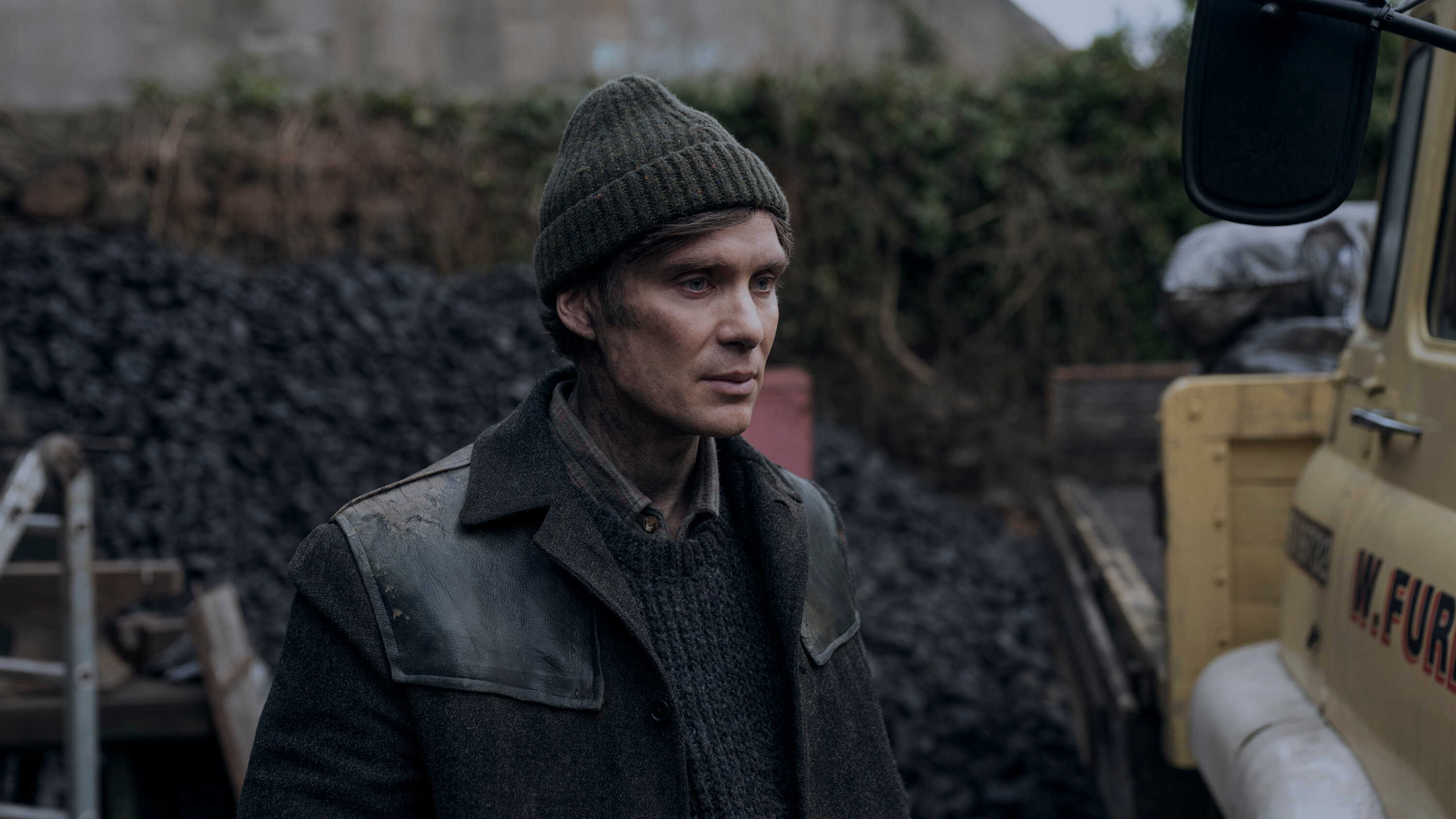 A man (Cillian Murphy) wearing a dark knit hat and coat next to a hill of rubble in Small Things Like This