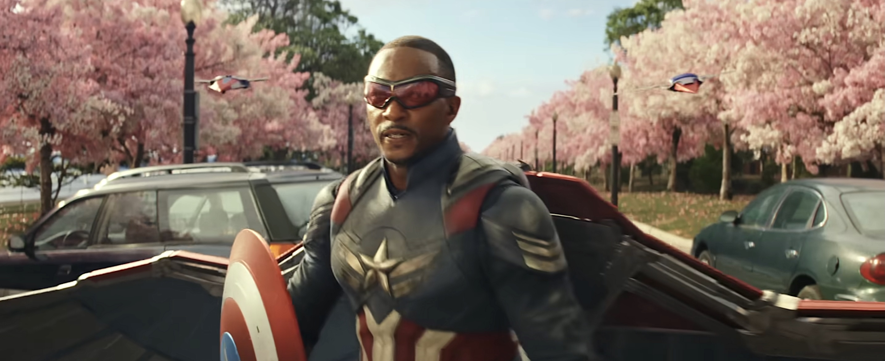Captain America (Anthony Mackie) stands in a park in full costume, surrounded by flowering cherry trees, in the trailer for Captain America: Brave New World