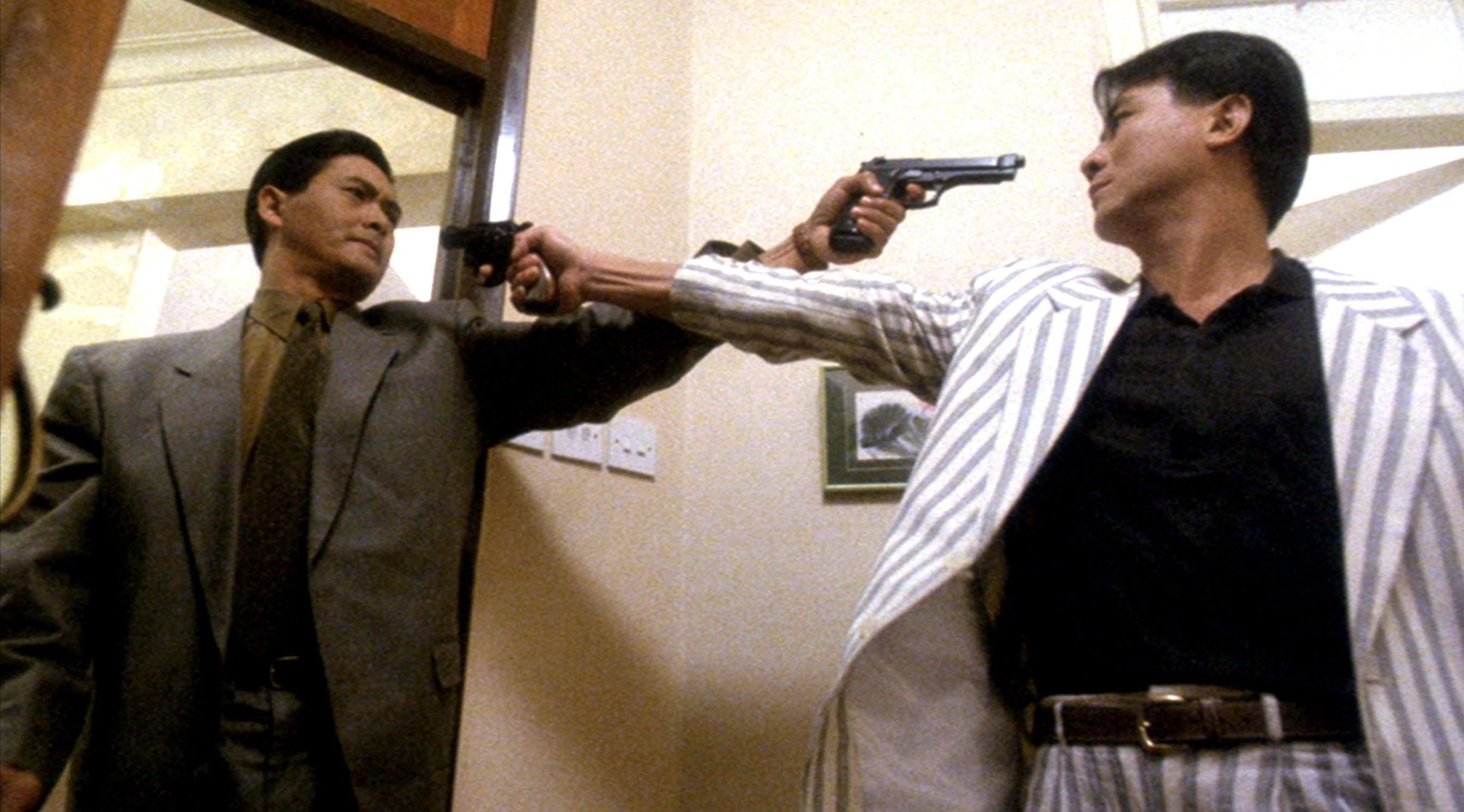 Chow Yun-fat and Danny Lee, both wearing suits, hold pistols in each others’ faces in The Killer
