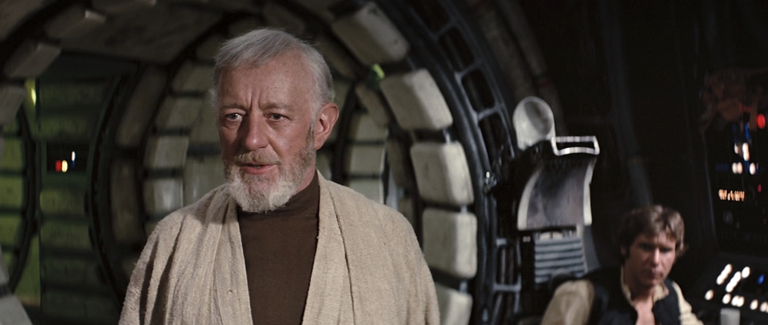 Alec Guinness as Obi-Wan Kenobi, standing in the Millennium Falcon with Han Solo (Harrison Ford) seated at a console in the background in Star Wars: Episode IV – A New Hope