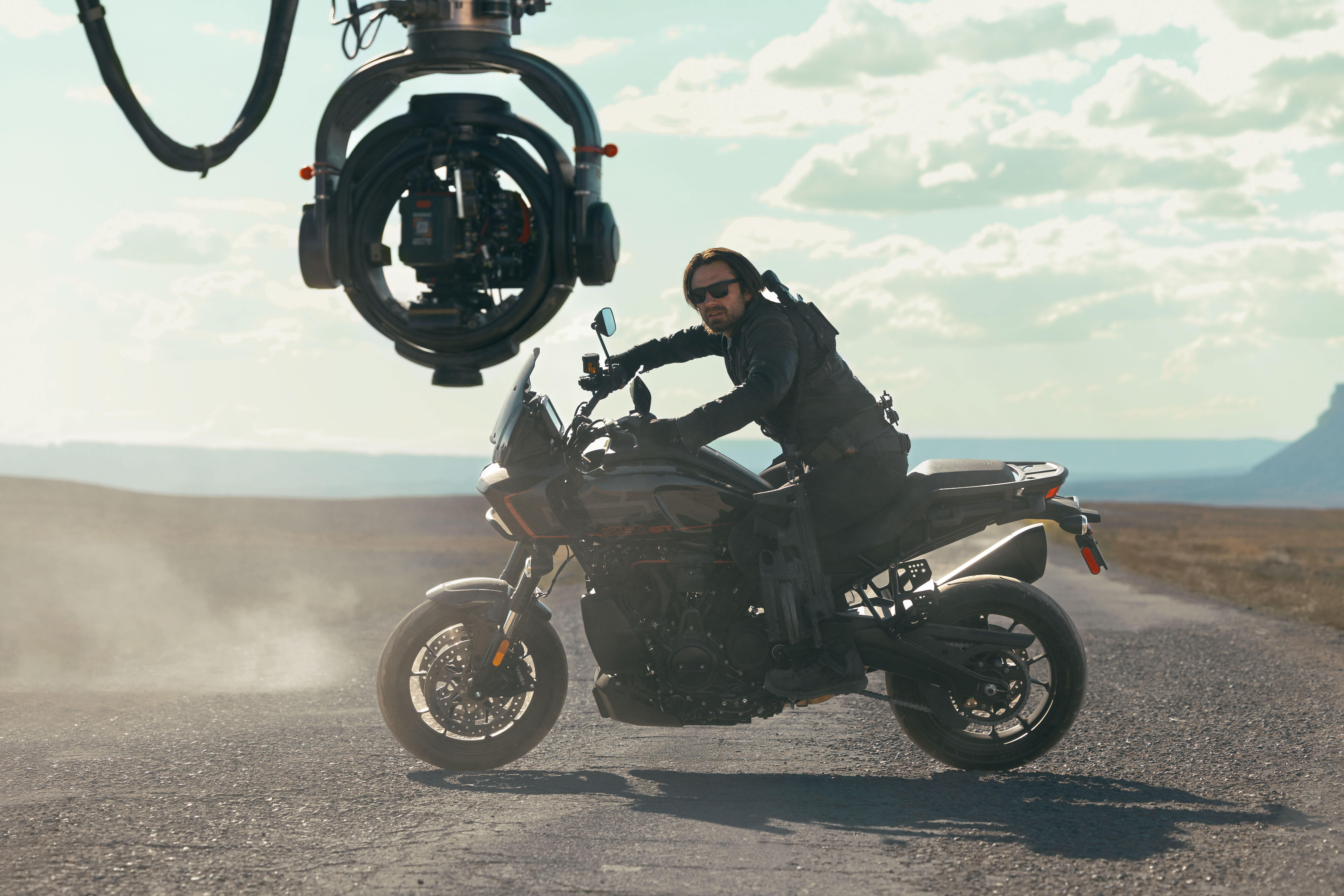 Sebastian Stan in character as Bucky Barnes, riding a motorcycle with a large camera in the foreground behind the scenes of Thunderbolts*