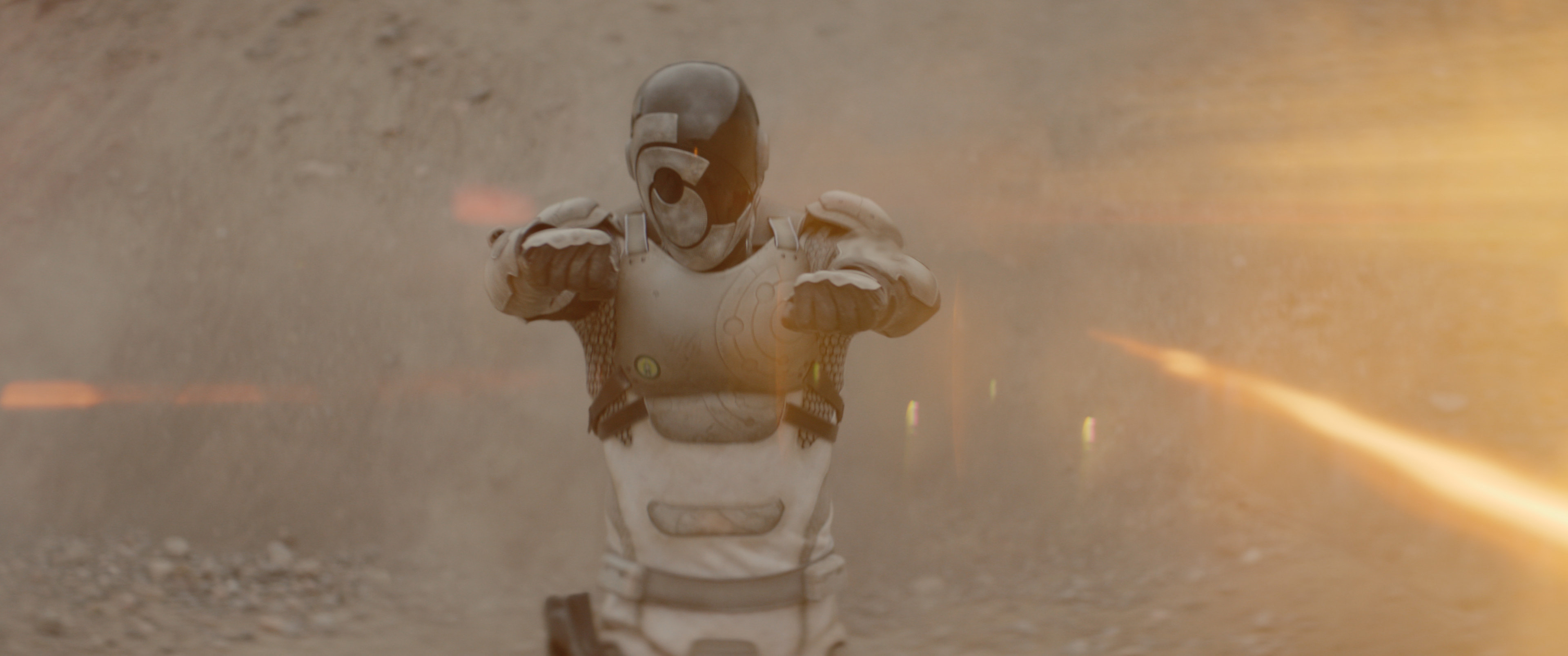 Murderbot (Alexander Skarsgård), a humanoid android in futuristic white body armor, charges toward the camera, fists up and wrist-guns active, surrounded by dust, in Apple TV Plus’ Martha Wells adaptation Murderbot