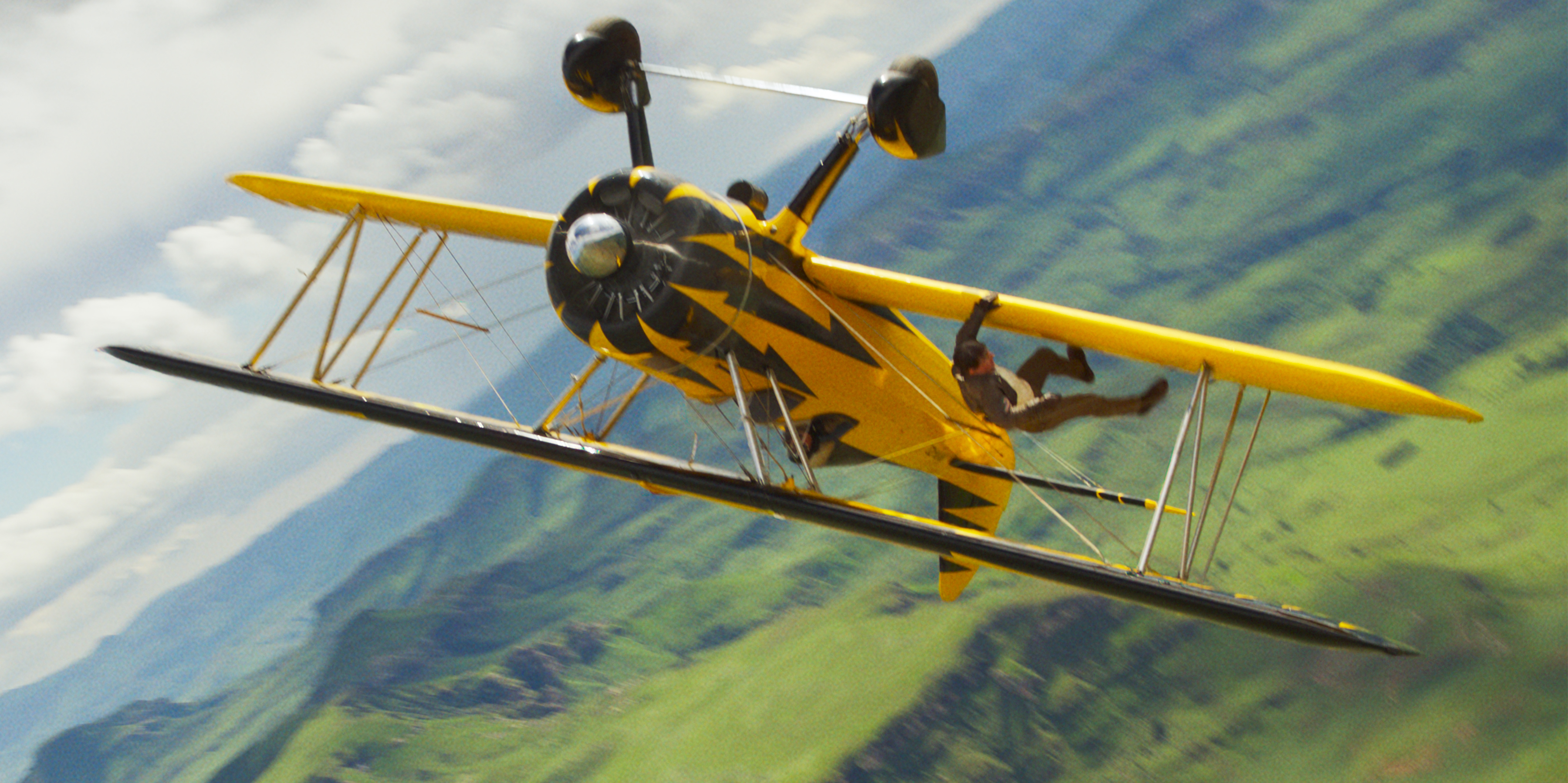 Ethan Hunt (Tom Cruise, and you can’t tell in this image, but given how he works, it’s probably really him) clings to the wing of an upside-down biplane high above the ground in Mission: Impossible — The Final Reckoning