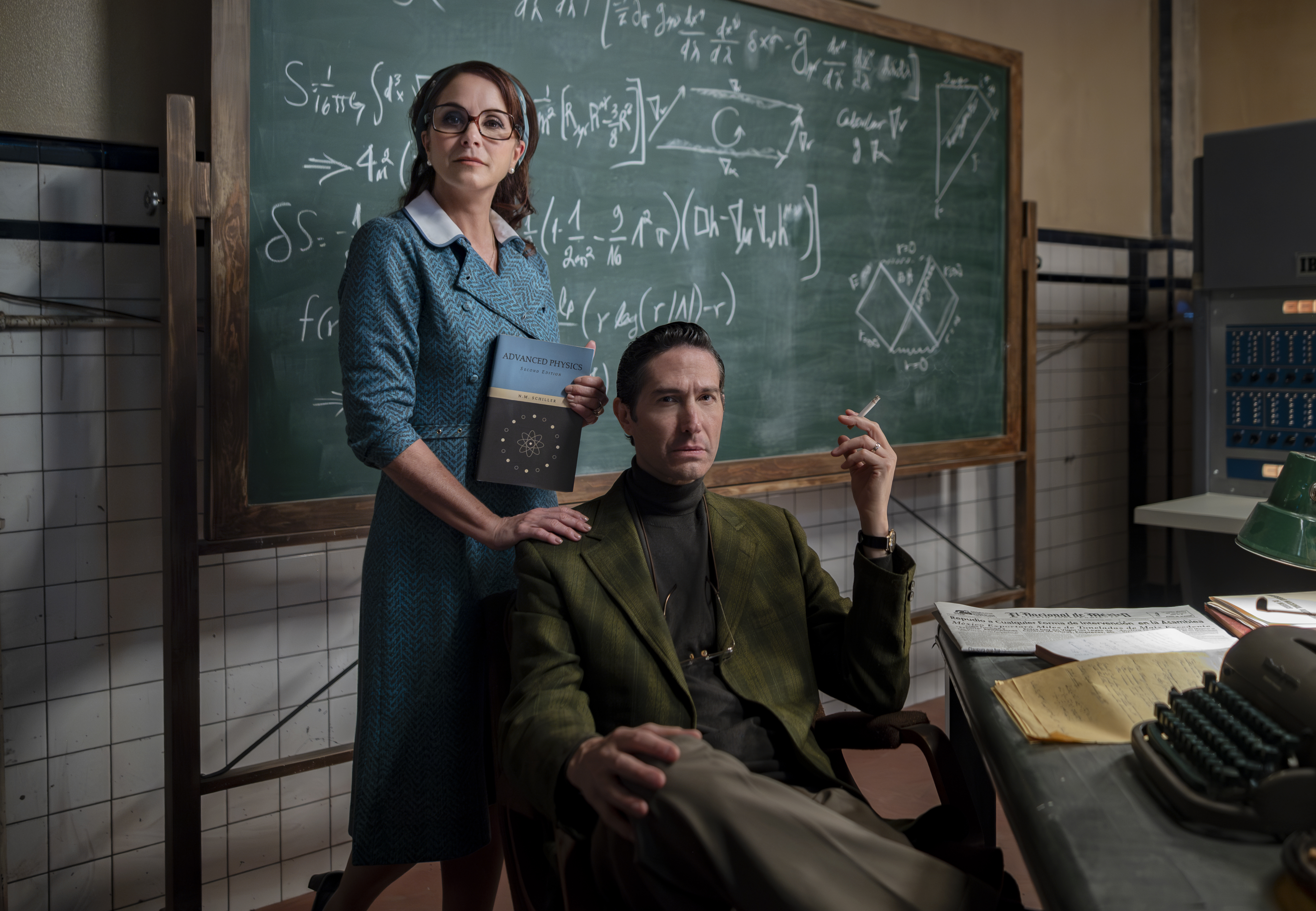 Lucero as Nora stands in front of a chalkboard with equations holding an advanced physics textbook with her hand on the shoulder Benny Ibarra playing her husband Héctor as he smokes a cigarette.